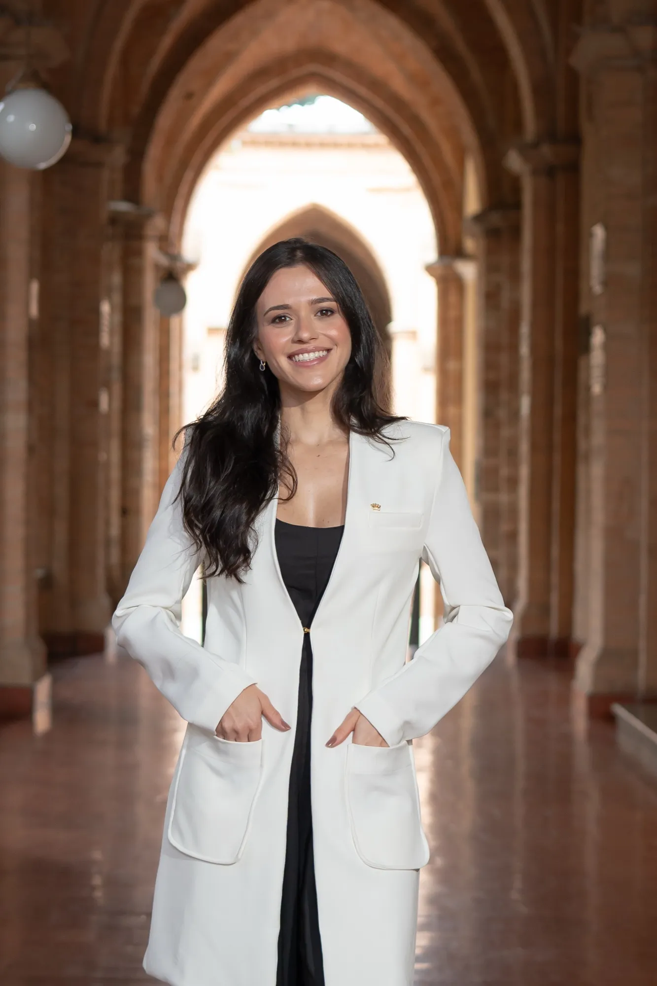Dra. Letícia Gaspar, dermatologista, de blazer branco sob arcos de tijolos