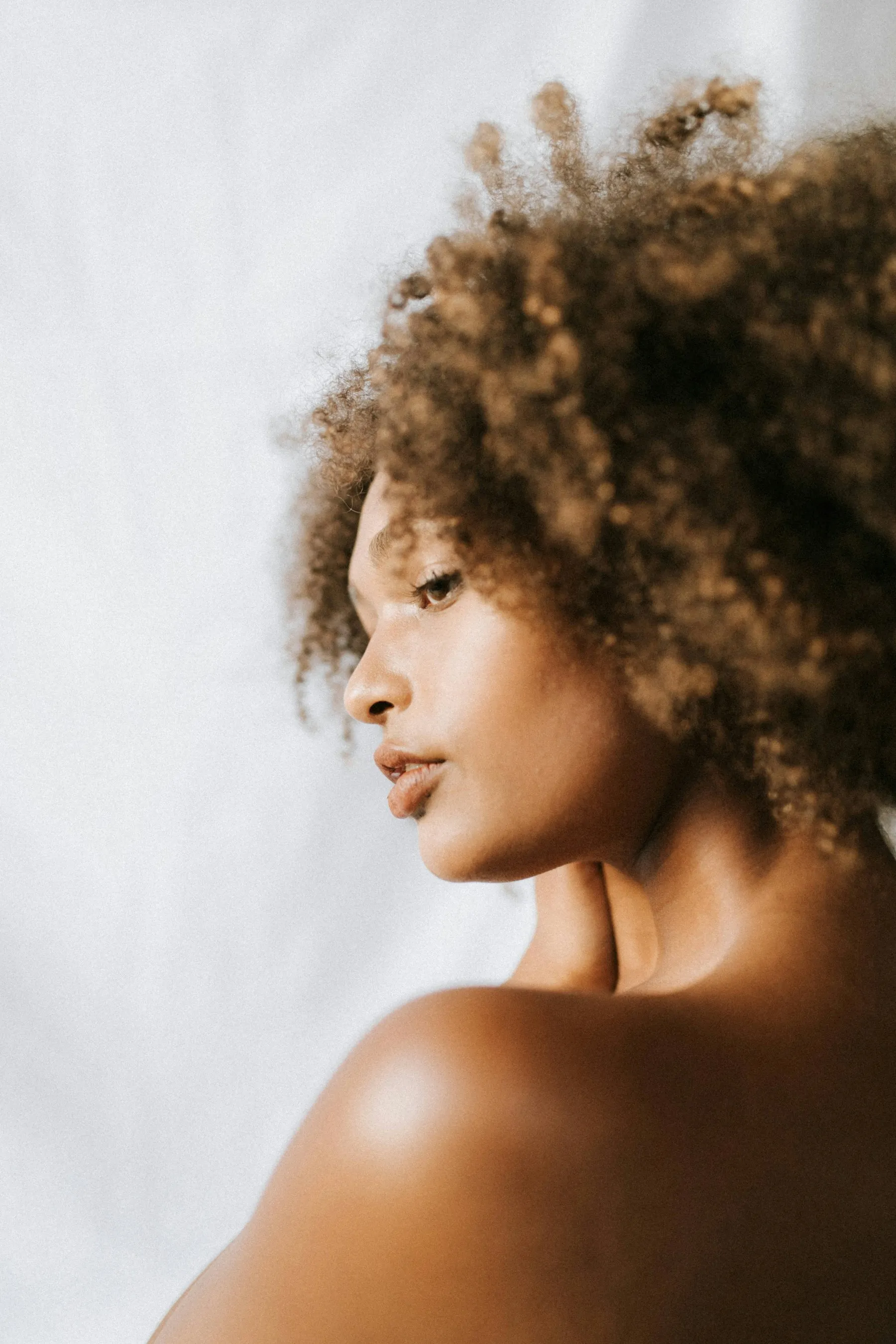 Perfil de mulher de cabelos cacheados, com a pele iluminada